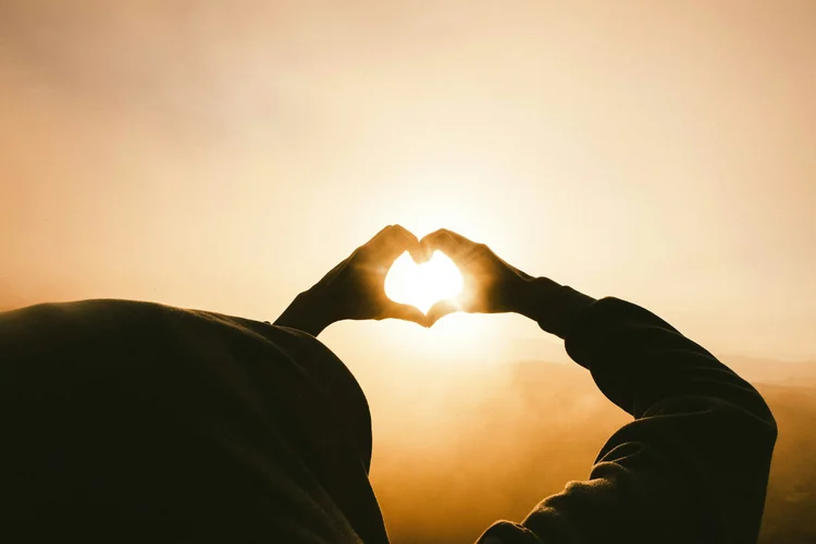 Hands forming a heart shape in front of the sun